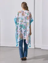 Kimono tejido con estampado floral multicolor, terminación de ruedo con borlas y mangas cortas con borde celeste.