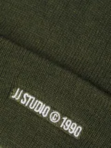 Gorro beanie verde oliva de punto, con logo bordado "JJ STUDIO © 1990" en blanco.
