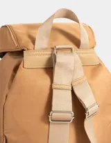 Mochila de tela color lila, con solapa con broche y tira de ajuste, doble bolsillo frontal con broche y pouch con charm lateral en forma de cartera.