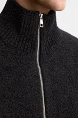 Cárdigan negro de punto con cuello subido, manga larga, bolsillos de vivo en cadera, acabados en rib y cierre frontal con cremallera.