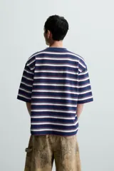 Camiseta de hombre a rayas horizontales azul marino, blancas y rojas, de corte holgado, cuello redondo y mangas cortas.