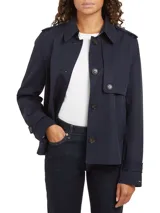 Gabardina corta azul marino de Tommy Hilfiger, con botonadura simple, cuello inglés, trabillas en los hombros, solapa de protección delantera y trasera, puños con tira y botón, y logo metálico en el puño.