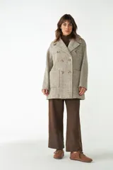 Abrigo de cuello solapa y manga larga, color beige con diseño de espiga. Cierre frontal cruzado doble con botones. Bolsillos delanteros plaqué, forrado al tono.