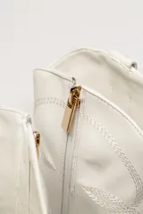 Bota corta de cuero sintético color blanco, estilo texana con bordados decorativos y taco cubano negro.