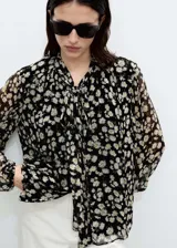Blusa de gasa negra con estampado de margaritas blancas, cuello pico con lazo y cierre de botones frontal.