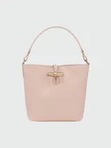 Bolso tipo bucket pequeño color rosa pálido, con asa corta y correa larga desmontable. Cierre superior con broche metálico dorado.