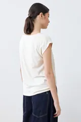 Blusa color beige con textura de lunares en relieve, cuello redondo y mangas cortas.