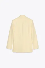 Blazer color crema confeccionado en hilatura con lino, de corte recto, con cuello solapa de muescas y manga larga acabada en abertura y botones. Tiene bolsillos delanteros y cierre frontal cruzado con botones.