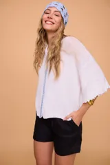 Saco tejido a máquina en lino y algodón color celeste, con silueta en línea A, mangas anchas, escote redondo con bordado en la delantera y botones de nácar. Largo por arriba de la cola.