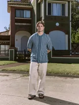 Polo de punto azul con rayas verticales blancas, cuello tipo camisa, cierre con botones y mangas cortas.