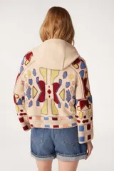 Sweater de punto beige con capucha y cordones burdeos. Presenta un diseño jacquard con motivos geométricos en azul, amarillo y rojo.