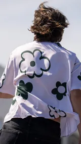 Camisa de manga corta, color blanco, con estampado de flores grandes en verde oscuro. Tiene cuello camisero y cierre frontal de botones.