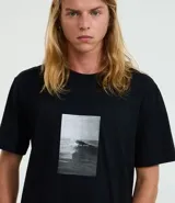 Remera negra de mangas cortas, confeccionada en media malla de algodón con cuello redondo y estampa photoprint de playa. Modelo cómodo de corte holgado.