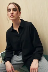 Camisa blanca de manga larga con textura sutil y caída fluida. Presenta cuello clásico, botones forrados a tono y puños con terminación fruncida.