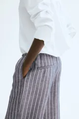 Pantalón recto de tela vaporosa a rayas verticales blancas sobre fondo gris. Tiene corte holgado, cintura elástica con cordón de ajuste, bolsillos laterales y traseros insertados.