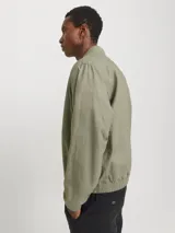 Campera bomber color verde claro, de tejido liviano de lino y algodón, con cuello tipo baseball, mangas largas con puños de canalé, cierre con cremallera y bolsillos delanteros.