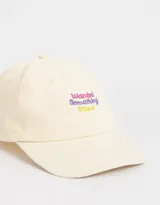 Gorra de béisbol color crema, de tela canvas, con visera curva y bordado frontal con la frase "Wanted Something More" en letras color lila y amarillo.