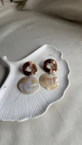 Par de aros colgantes con diseño circular, uno marrón con centro calado y otro blanco con efecto nacarado.