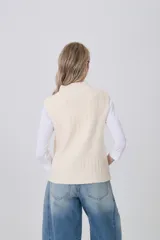 Chaleco de punto color crema, sin mangas, con cuello alto y textura acanalada vertical.