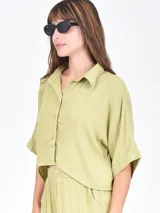 Camisa negra de manga corta con cuello camisero y botones frontales. Presenta un corte cropped y textura acanalada o plisada.