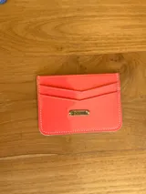 Tarjetero azul de cuero charol con tres ranuras para tarjetas y logo de la marca grabado en una placa dorada.