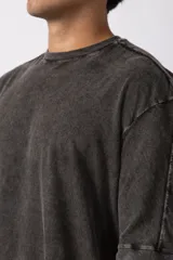 Remera oversize de algodón pesado, color gris oscuro con efecto lavado 'snow' que le da un aspecto gastado y único. Presenta cuello redondo y costuras vistas en hombros y mangas.
