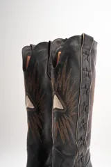 Botas texanas de cuero color marrón con bordados de estrellas y rayos de sol en color blanco. Tiene un pequeño taco de madera y detalles en rojo en el borde superior.