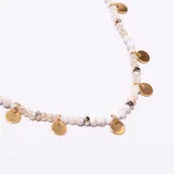 Gargantilla tipo choker compuesta por pequeñas cuentas facetadas de color blanco o crema, con pequeños dijes metálicos dorados en forma de moneda colgando a lo largo de la cadena. Posee un cierre de mosquetón y cadena de ajuste en tono dorado.