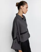 Camisa gris con bordados negros, de corte holgado y mangas anchas.