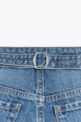 Bermuda de denim azul de tiro medio con cinco bolsillos, trabilla ajustable en la espalda, bajo sin costuras y cierre frontal con botones metálicos.