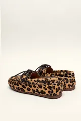 Mocasín tipo boat shoe con estampado de vaca en tonos marrón y blanco, confeccionado en cuero. Cuenta con cordones de cuero marrón oscuro y suela de goma.