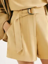 Short de vestir color beige, de corte recto y tiro alto, con pliegues frontales, bolsillos laterales y un cinturón de tela a juego con hebilla oscura.