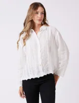 Camisa de algodón blanca con bordados florales verticales, cuello con solapa y cierre frontal con botones.