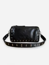 Bandolera negra de cuero con tachas plateadas. Tiene dos asas desmontables: una corta con tachas para llevarla en la mano o al hombro, y una larga para llevarla al hombro o cruzada.
