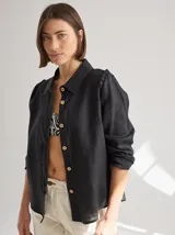 Camisa negra de lino con cuello clásico, abotonada al frente y mangas largas con volados en los hombros.