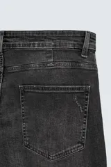 Pantalón de jean negro ajustado al cuerpo desde la cintura hasta el tobillo, de tiro medio y tejido elástico. Diseño de cinco bolsillos con lavado efecto roto y cierre frontal con cremallera y botón.
