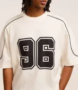 Remera de corte boxy color crema con estampa del número 96 en el frente y detalles en negro en cuello y mangas.