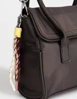 Cartera tipo city color beige, de tela deportiva, con doble asa corta, correa regulable desmontable, solapa con broche a presión y charm colgante.
