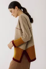 Sweater beige de lana con mangas 3/4, corte holgado, detalle de costuras rojas y bolsillo pequeño en el pecho.