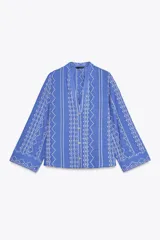 Camisa azul con bordados blancos, de cuello redondo con escote pico y manga larga.