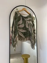 Blusa verde con estampado de hojas beige, cuello redondo y corte asimétrico.
