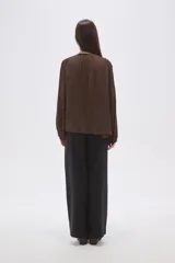 Blusa holgada color crema, confeccionada en viscosa, con frunces en el canesú superior y cuello en V con cordón ajustable terminado en mostacillas. Posee cierre frontal de botones y mangas largas abullonadas.