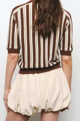 Falda pantalón corta color crudo, de tiro medio, con cintura elastizada y detalle de tejido con volumen y pliegues.