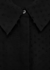 Camisa negra de plumeti con cuello camisero, manga larga con puños abotonados y cierre frontal de botones oculto.