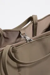 Bolso shopper grande de nylon negro, con estructura blanda, doble asa de mano y correa larga ajustable para llevar al hombro. Presenta un logo metálico con el texto "BIMBA Y LOLA" en la parte frontal inferior.