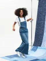 Jumper largo de denim azul con breteles regulables, bolsillos frontales y corte recto.