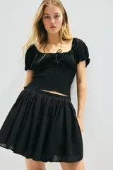 Blusa negra con escote cuadrado, mangas cortas abullonadas con elástico en hombros y puños, cintura fruncida y abertura con cordón para ajustar en el delantero.