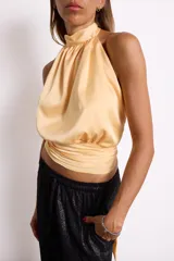 Blusa color amarillo pálido con cuello halter y corte irregular en la cintura.