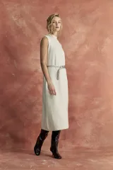 Vestido midi color beige, sin mangas y cuello alto. Incluye cinturón de cadena plateada con dije de cuero marrón.
