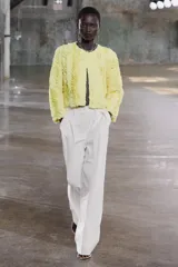 Chaqueta corta color amarillo pastel con textura de volantes, cuello redondo, manga larga y cierre frontal con botón a presión oculto.